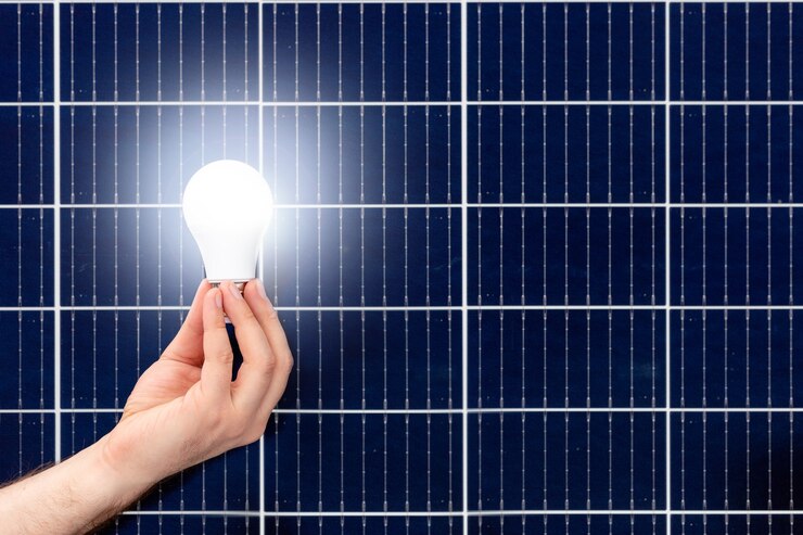 Hand hält weiße Glühbirne gegen Sonnenkollektor, Solarstation. Ideenkonzept der alternativen Energie, Technologie, Umwelt, Ökologie. Grüne Energie. Platz kopieren.