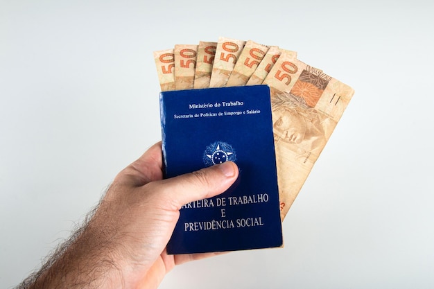 Hand halten brasilianische Dokumentenarbeit und soziale Sicherheit Carteira de Trabalho e Previdencia Social mit fünfzig Reais Banknoten brasilianisches Geld