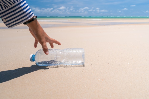 Hand heben leere Wasserflasche oder Müll am schönen Strand auf. Umwelt Problem der globalen Erwärmung.
