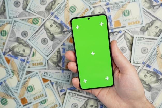Hand holding smartphone com tela verde em pilha de notas de dólar vista superior
