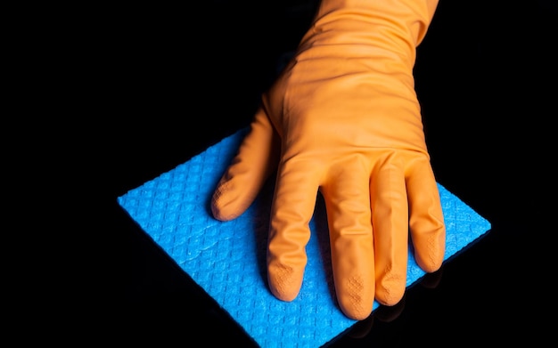 Hand im Handschuh reinigt einen schwarzen Tisch mit einer blauen Serviette Nahaufnahme des Reinigungsprozesses zu Hause