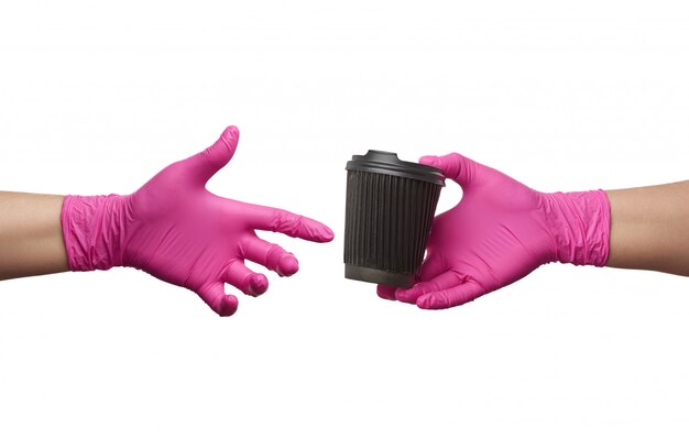 Hand in einem rosa Latexhandschuh hält einen Einwegkartonbecher aus Papier