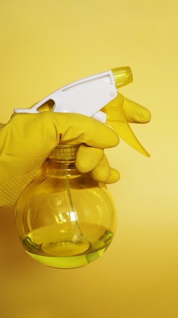 Hand in gelbem Gummihandschuh mit Plastiksprühflasche mit Reinigungsmittel auf gelbem Hintergrund - vertikal