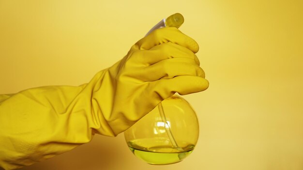 Hand in gelben Gummihandschuh mit Plastiksprühflasche mit Reinigungsmittel auf gelbem Hintergrund