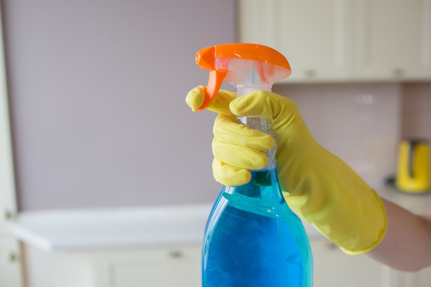 Hand in gelben Handschuh hält Sprühflasche mit blauer Flüssigkeit. Der Finger drückt auf den Haken.