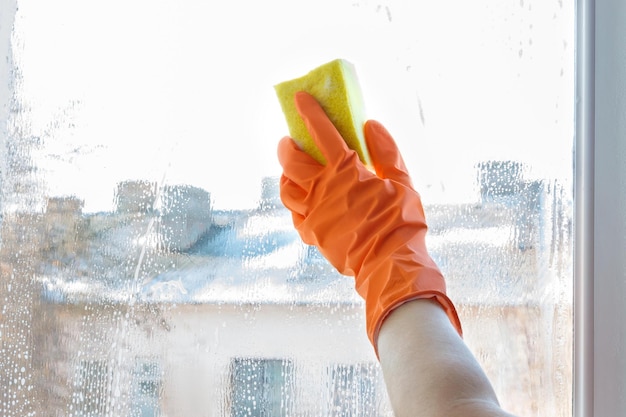 Hand in Gummihandschuh wäscht ein Fenster