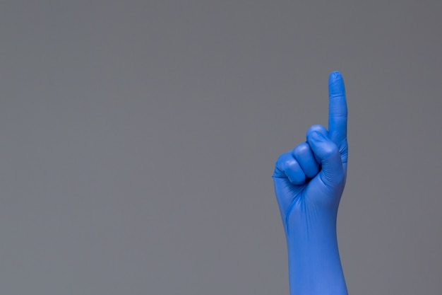Hand in Gummihandschuh zeigt mit dem Zeigefinger nach oben, copyspace.