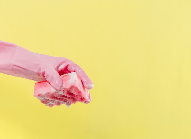 Hand in rosa Gummihandschuhen hält einen Seifenschwamm Gelber Hintergrund Hauswirtschaft und Reinigung