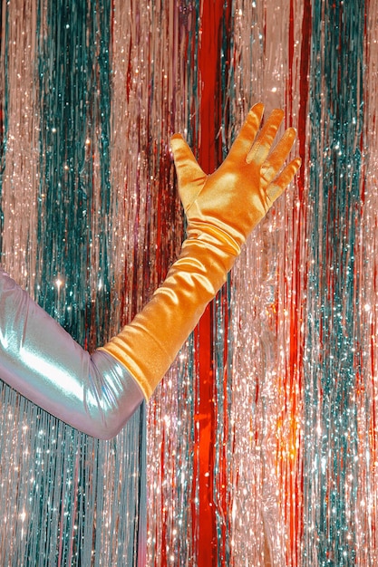 Hand in Vintage goldene Handschuhe, Lametta Hintergrund. Clubbing-Stimmung des neuen Jahres. Frohe Weihnachten. Urlaub. Mode und glänzen wie Sterne. Retro-Party-Konzept