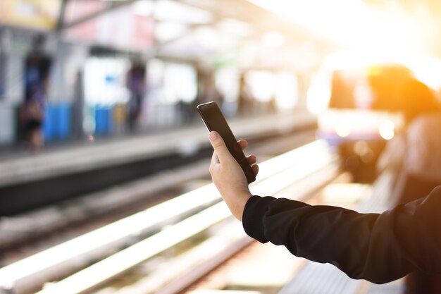 Hand ist benutzter schwarzer Smartphone auf der Bahnstation mit Zughintergrund