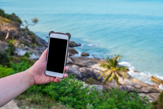 Hand junge frauen mit smartphone-handy entspannen auf blick auf das blaue meer im morgenlicht