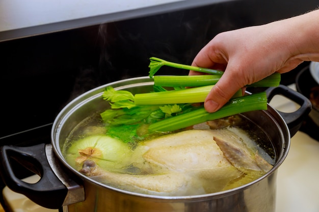 Hand legt Sellerie mit ganzem Huhn in den Topf