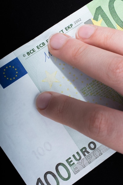 Hand mit 100-Euro-Banknote auf schwarzem Hintergrund