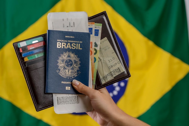 Hand mit brasilianischem Pass mit brasilianischer Flagge im verschwommenen Hintergrund