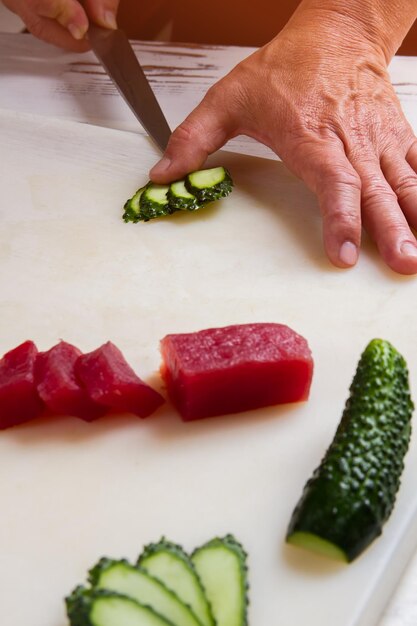 Hand mit dem Messer, das Gurkenscheiben von rotem Fischfleischrestaurantkoch am Arbeitsgemüse für Japan schneidet...