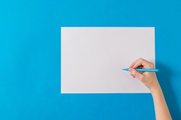 Hand mit einem blauen Marker mit einem weißen Blatt Papier auf blauem Hintergrund