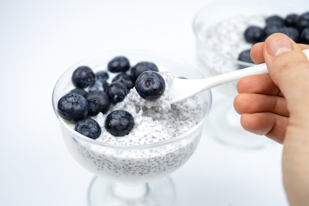 Hand mit einem Löffel, der gesundes Frühstück mit Joghurt, Chiasamen und Blaubeere aufhebt.