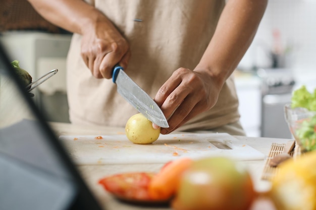 Hand mit einem Messer schneidet Zitrone auf dem Schneidbrett, um Gemüsesalat in der Küche herzustellen