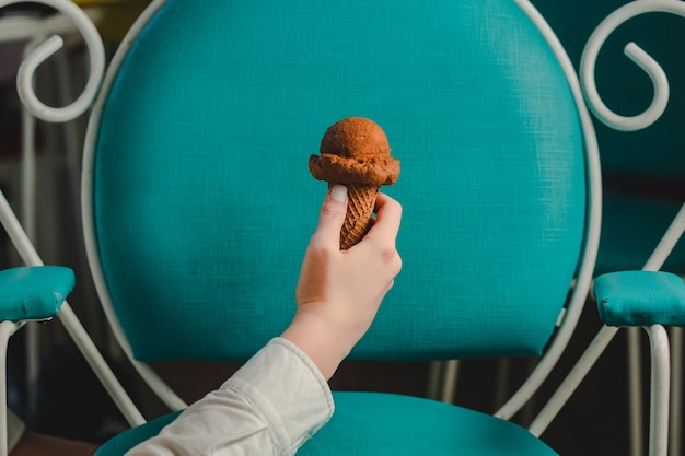 Hand mit einem Schokoladenkegel mit einem blauen Vintage-Stuhl auf der Rückseite