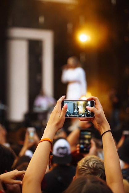 Hand mit einem Telefon zeichnet Live-Musikfestival auf Menschen, die mit Smartphones fotografieren