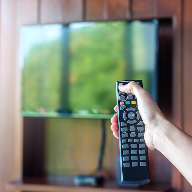 Hand mit Fernbedienung zum Einstellen von Smart TV im modernen Zimmer zu Hause oder im Luxushotel