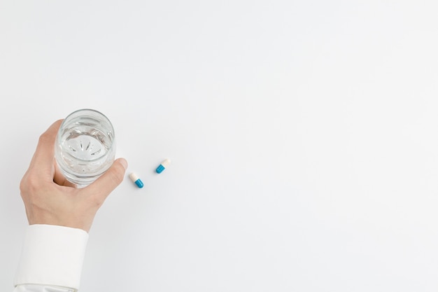 Hand mit Glas Wasser und Pille weißer Hintergrund