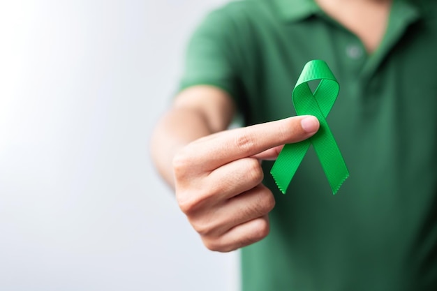 Hand mit grünem Band für Leber Gallenblase Gallengang Halsniere Krebs und Lymphom Awareness Month Konzept für das Gesundheitswesen und den Weltkrebstag