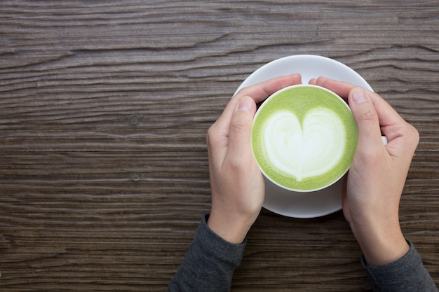 Hand mit grünem Tee Latte auf hölzernem Hintergrund