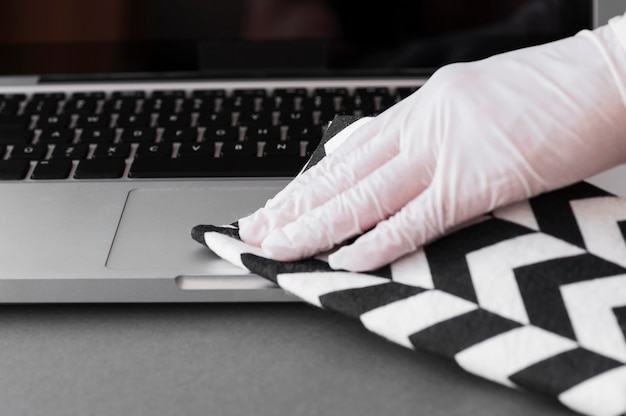 Hand mit Handschuh desinfizieren Laptop Oberfläche