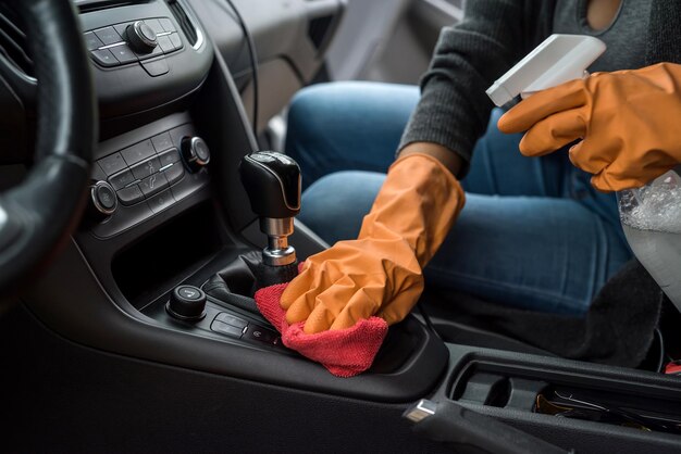 Hand mit Handschuh mit Feuchttuch und antibakteriellem Spray zum Reinigen des Autoinnenraums