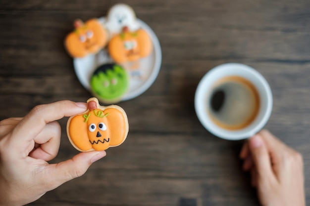 Hand mit Kaffeetasse beim Essen lustiger Halloween-Plätzchen Happy Halloween Day Trick or Threat Hallo Oktober Herbst Herbst Traditionelles Party- und Urlaubskonzept