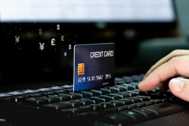 Hand mit Kreditkarte auf Tastatur mit Geldwährungssymbolfluss.