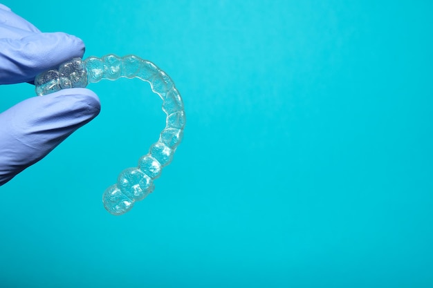 Hand mit lila Handschuh mit transparentem Zahnhalter auf blauem Hintergrund