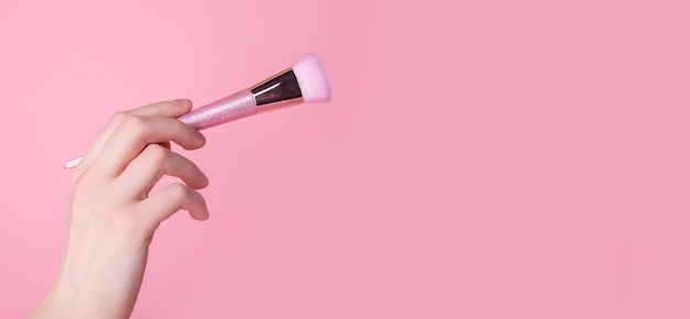 Hand mit Make-up-Pinsel auf rosa Hintergrund Werbebanner mit Kopierbereich