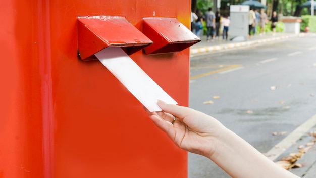 Hand mit Postkarte und Drop in roten Postkasten