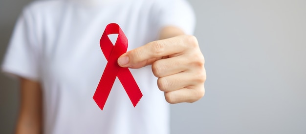 Hand mit rotem Band für den Welt-Aids-Tag im Dezember (erworbenes Immunschwächesyndrom), den Monat des Bewusstseins für multiples Myelom und die Nationale Rote Schleife-Woche. Konzept des Gesundheitswesens und des Weltkrebstages