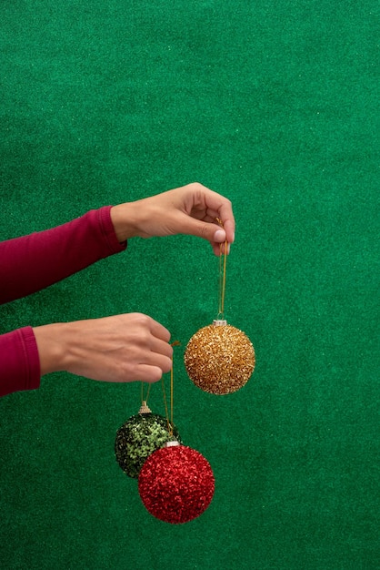 Hand mit roten, grünen und goldenen Weihnachtskugeln auf einem glänzenden grünen Hintergrund