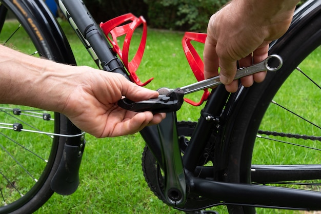 Hand mit Schraubenschlüssel, der Fahrradpedale auf dem Gras befestigt