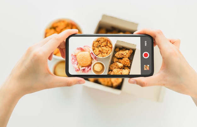 Hand mit Smartphone mit Fast-Food-Brathähnchen-Fotografie.