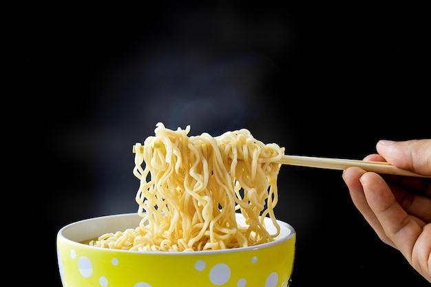 Foto hand mit stäbchen, nudeln mit dampf und rauch in einer schüssel auf schwarzem hintergrund. draufsicht, asiatisches essen auf dem tisch, food-konzept