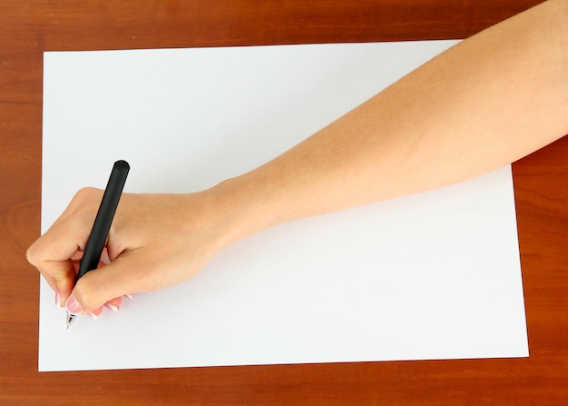 Hand mit Stift auf weißem Papier auf hölzernem Hintergrund