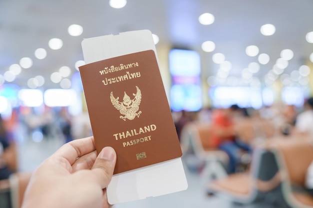 Hand mit thailändischem Pass und Bordkartenticket im internationalen Flughafen Reiseurlaub und Transportkonzepte