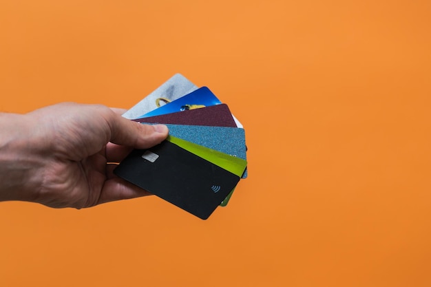 Hand mit vielen Kreditkarten mit Kopienraum auf orangefarbenem Hintergrund