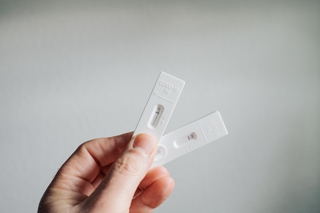Hand mit zwei negativen COVID-19-Ergebnissen und einem Testkit für virale Krankheiten