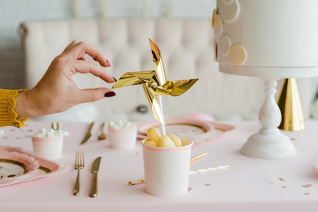 Hand nahe goldenem Windrad im Pappbecher auf dekorativem Partytisch für Mädchengeburtstag