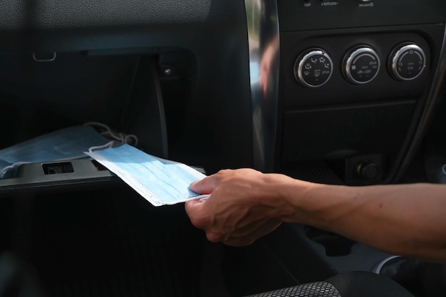 Hand nimmt eine medizinische Maske aus dem Handschuhfach im Auto