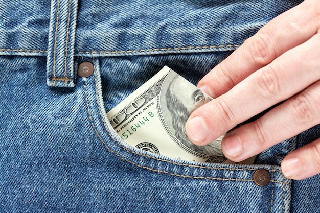 Hand nimmt oder steckt US-Dollar-Banknoten in die rechte Vordertasche von Blue Jeans Konzept, Geld oder Taschenkosten zu sparen