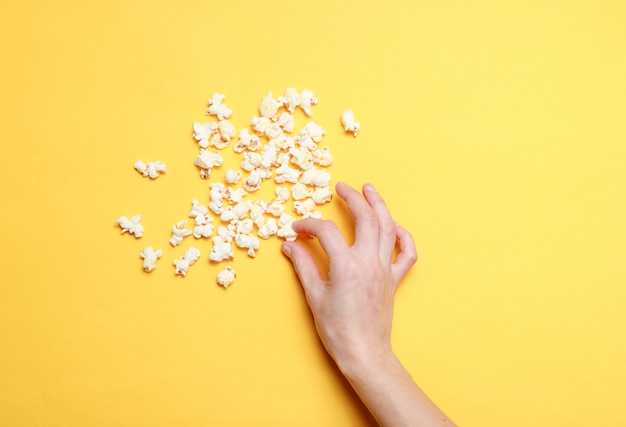 Hand nimmt Popcorn auf gelb. Draufsicht.