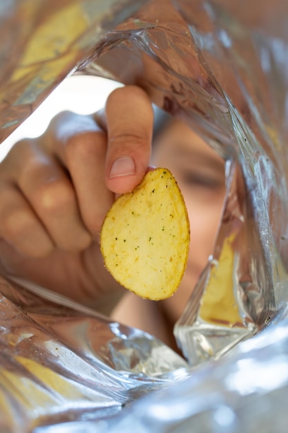 Hand pflückt Kartoffelchips aus dem Snack-Beutel und öffnet ein Paket mit Chips