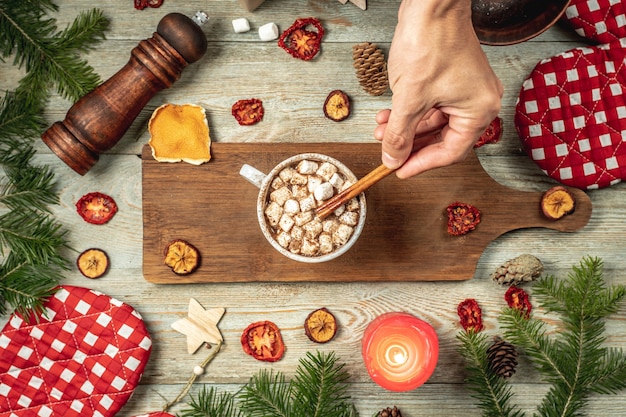 Hand rührt heiße Schokolade mit Marshmallows mit einer Zimtstange. Konzept der gemütlichen Neujahrs- und Weihnachtsstimmung. Ansicht von oben